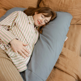 Pregnant woman lying comfortably with the MINICAMP U-shaped pregnancy pillow in stone grey