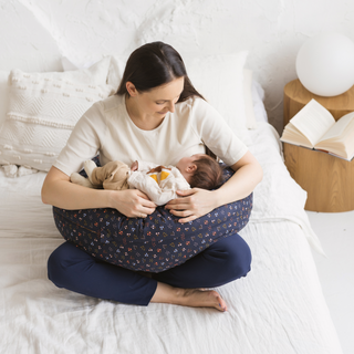 Woman using C-shape comfort pillow while nursing a baby in a cosy bedroom